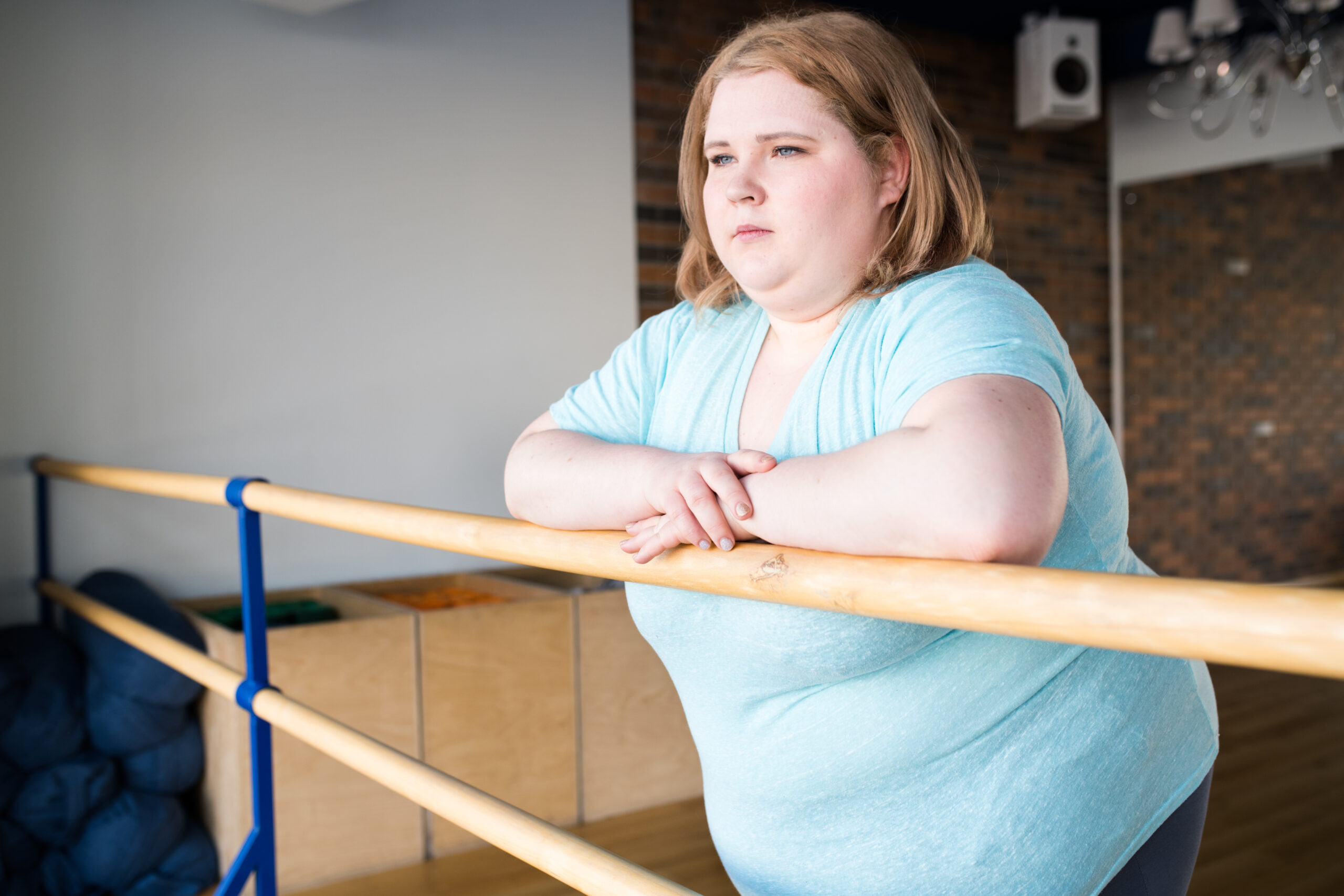 Obese person thinking while leaning against a wooden handrail.