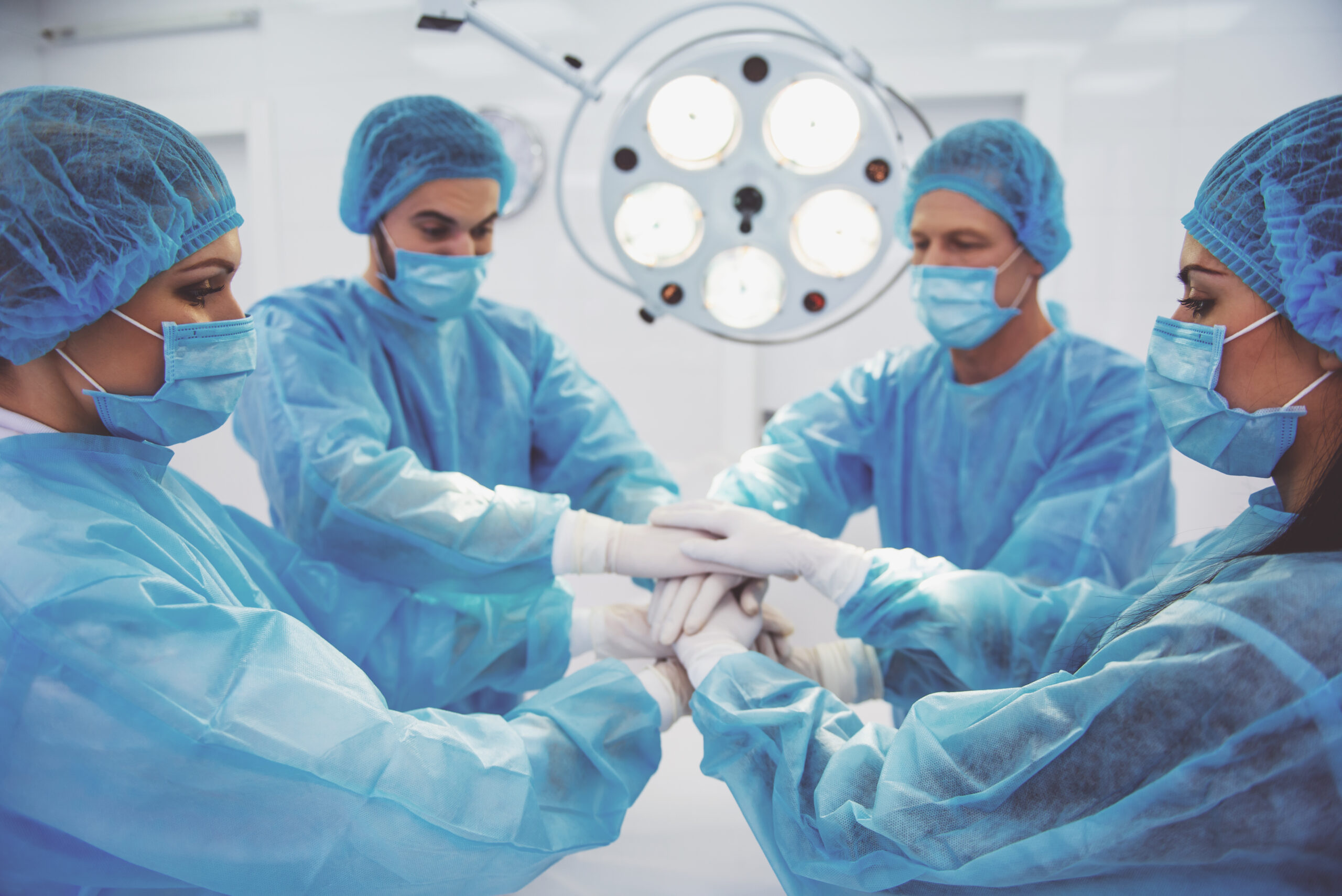 Team surgeons are putting their hands together, standing in a modern operating room