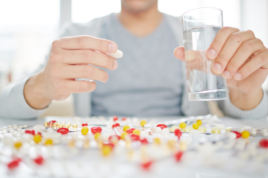 Hands of a man drinking a glass of water and its vitamins.