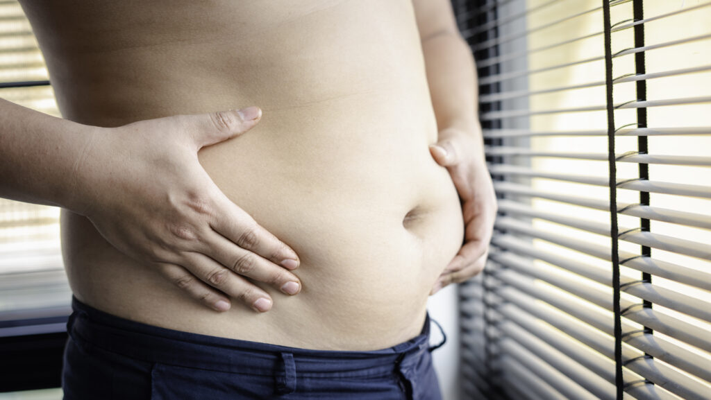 Obese person holding her belly, next to the window